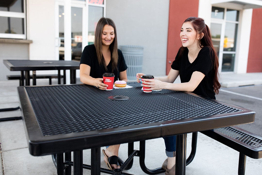 2 women sit at a Rise and Roast on a Regal Square Portable Table.